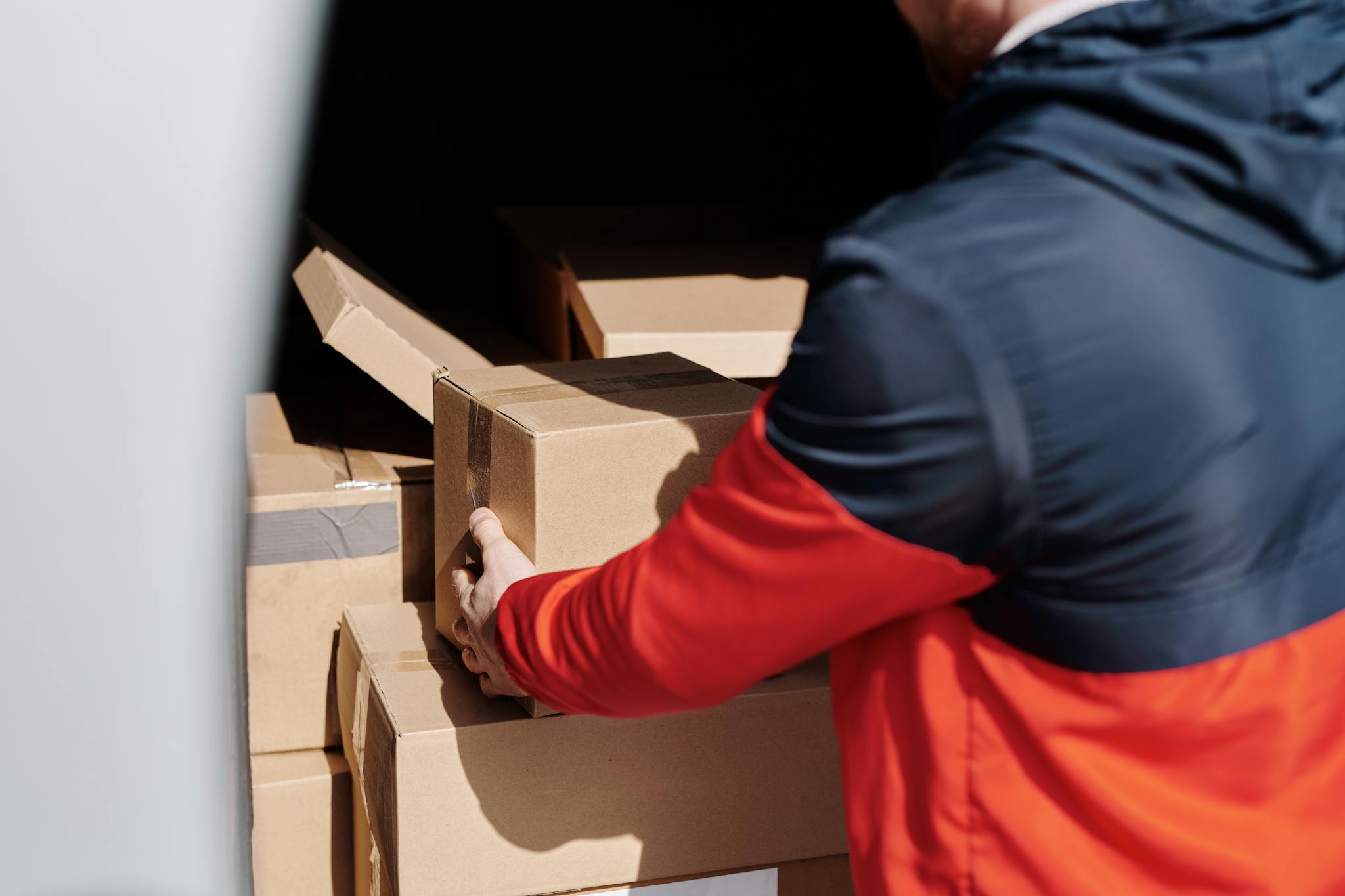 A delivery worker efficiently loads cardboard boxes into a vehicle for shipment.